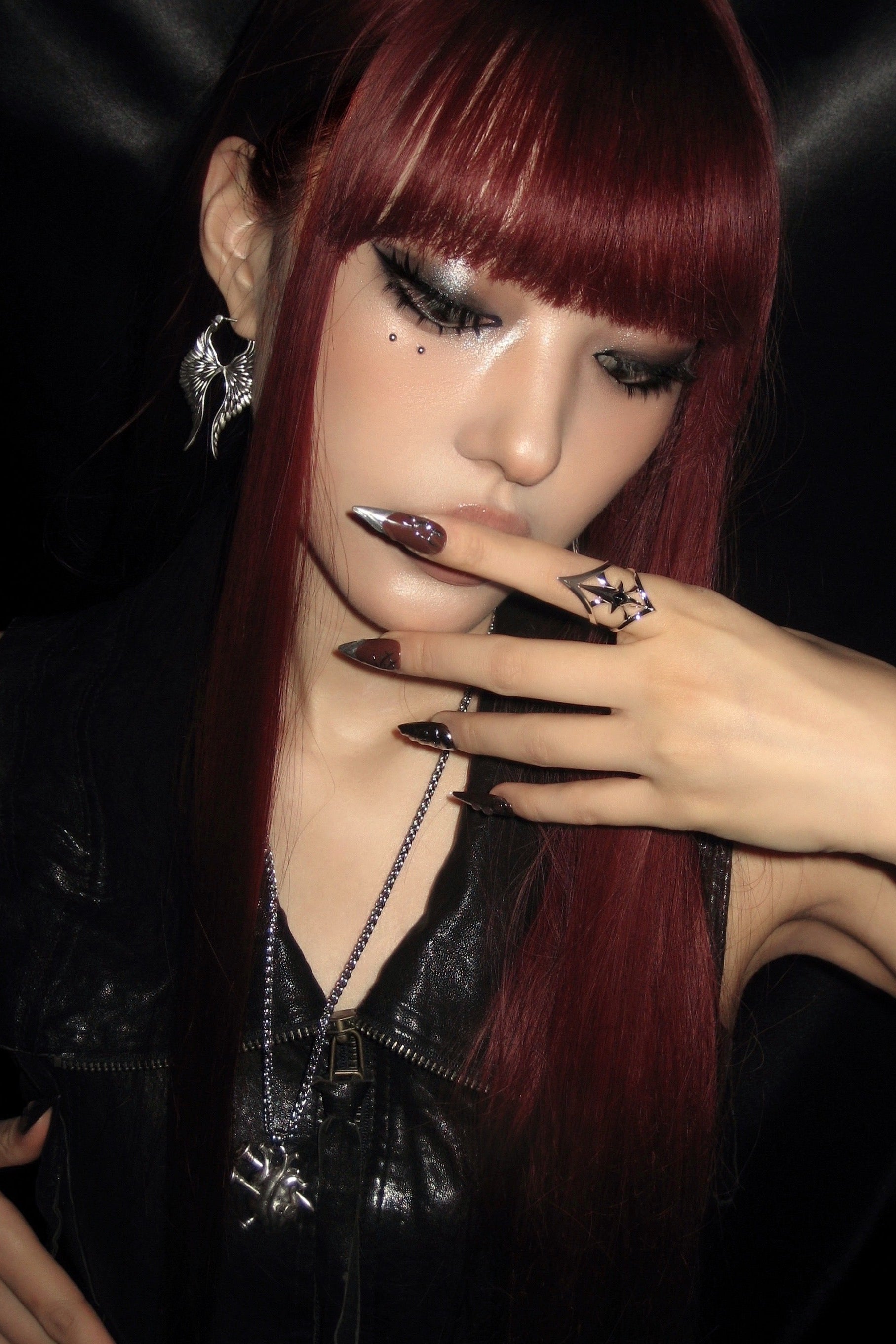 Woman with red hair and dark makeup wearing a black leather outfit against a dark background