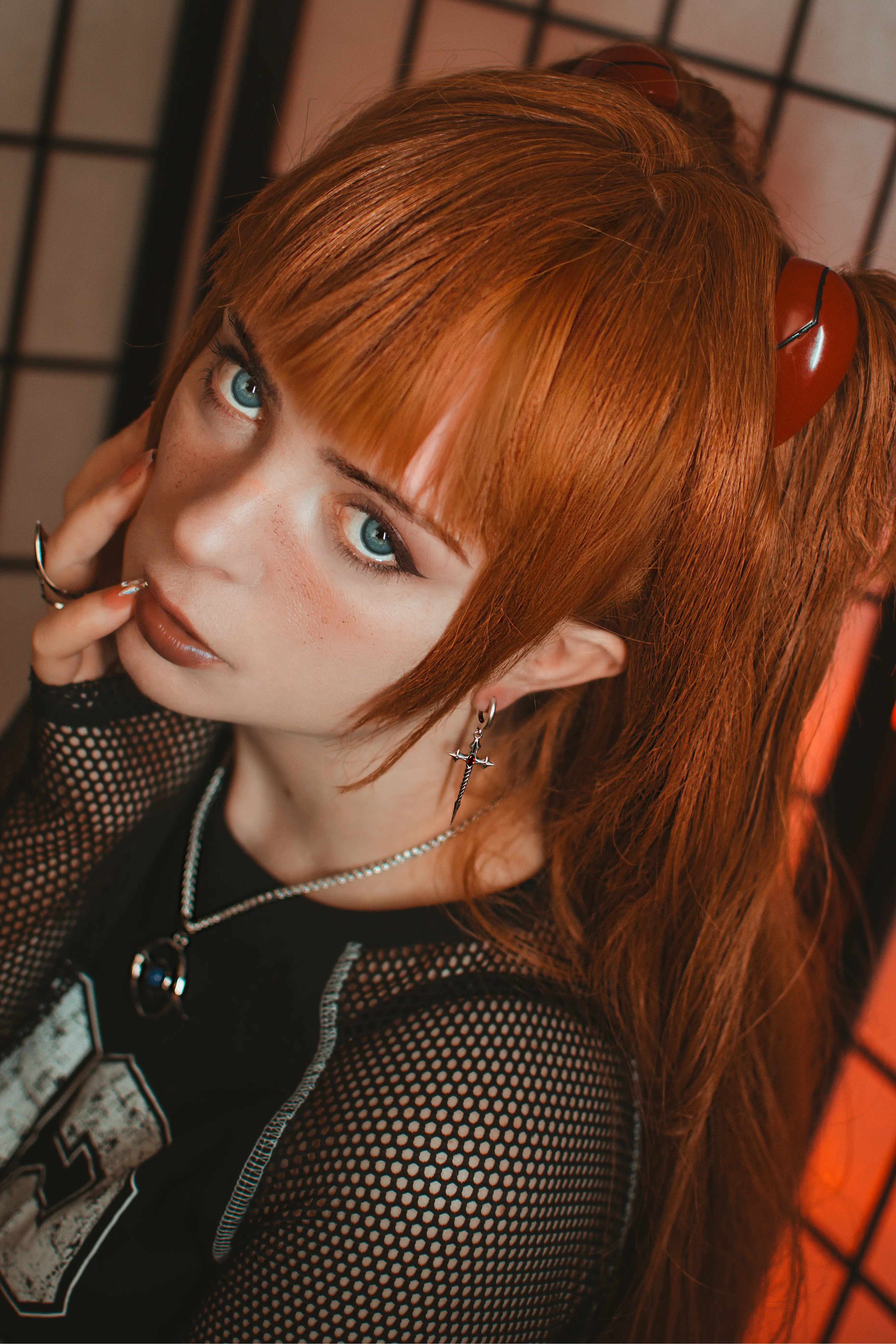 Person with red hair styled in pigtails, wearing a black mesh top and multiple necklaces.