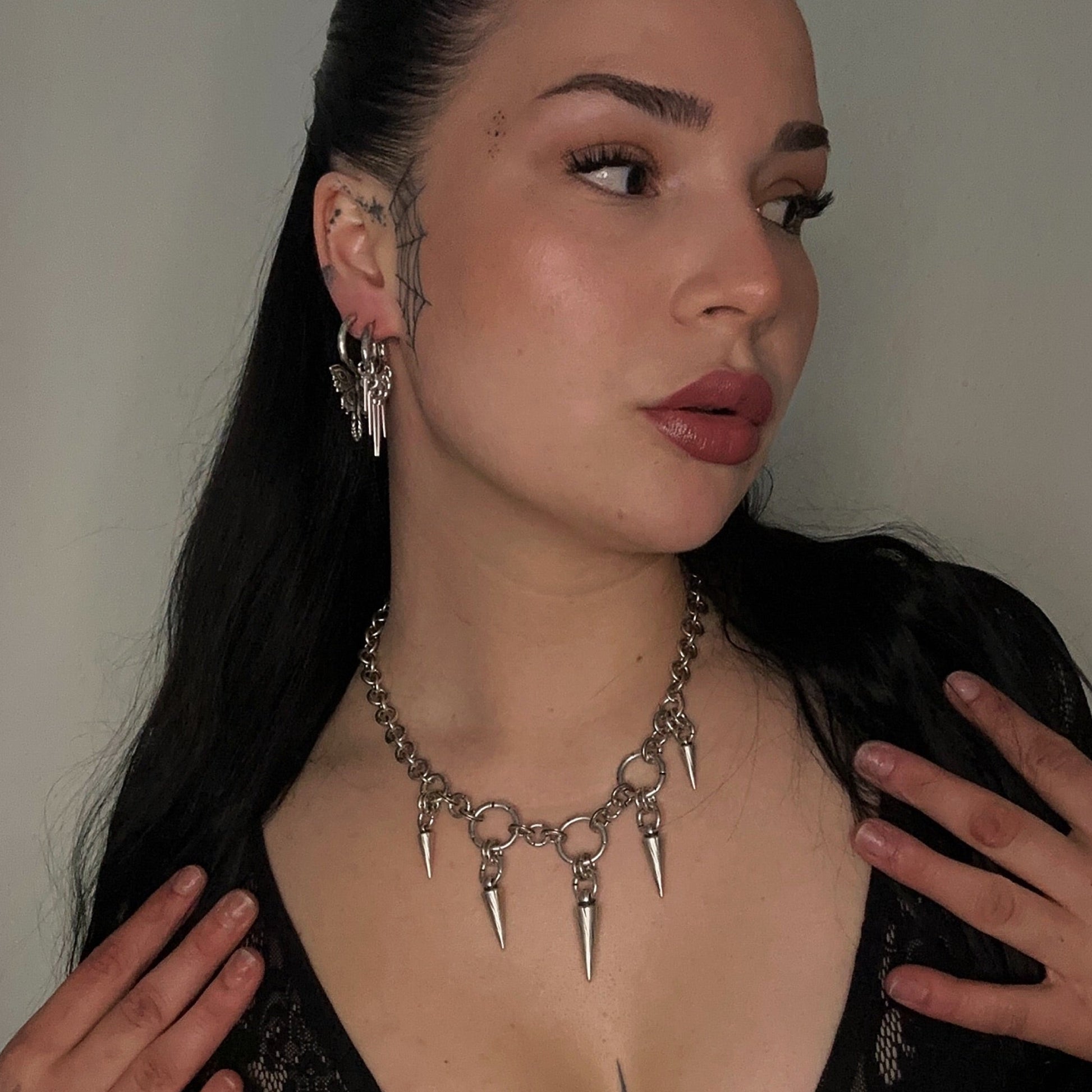 Woman wearing a black top with a deep neckline and a metallic necklace with sharp elements.
