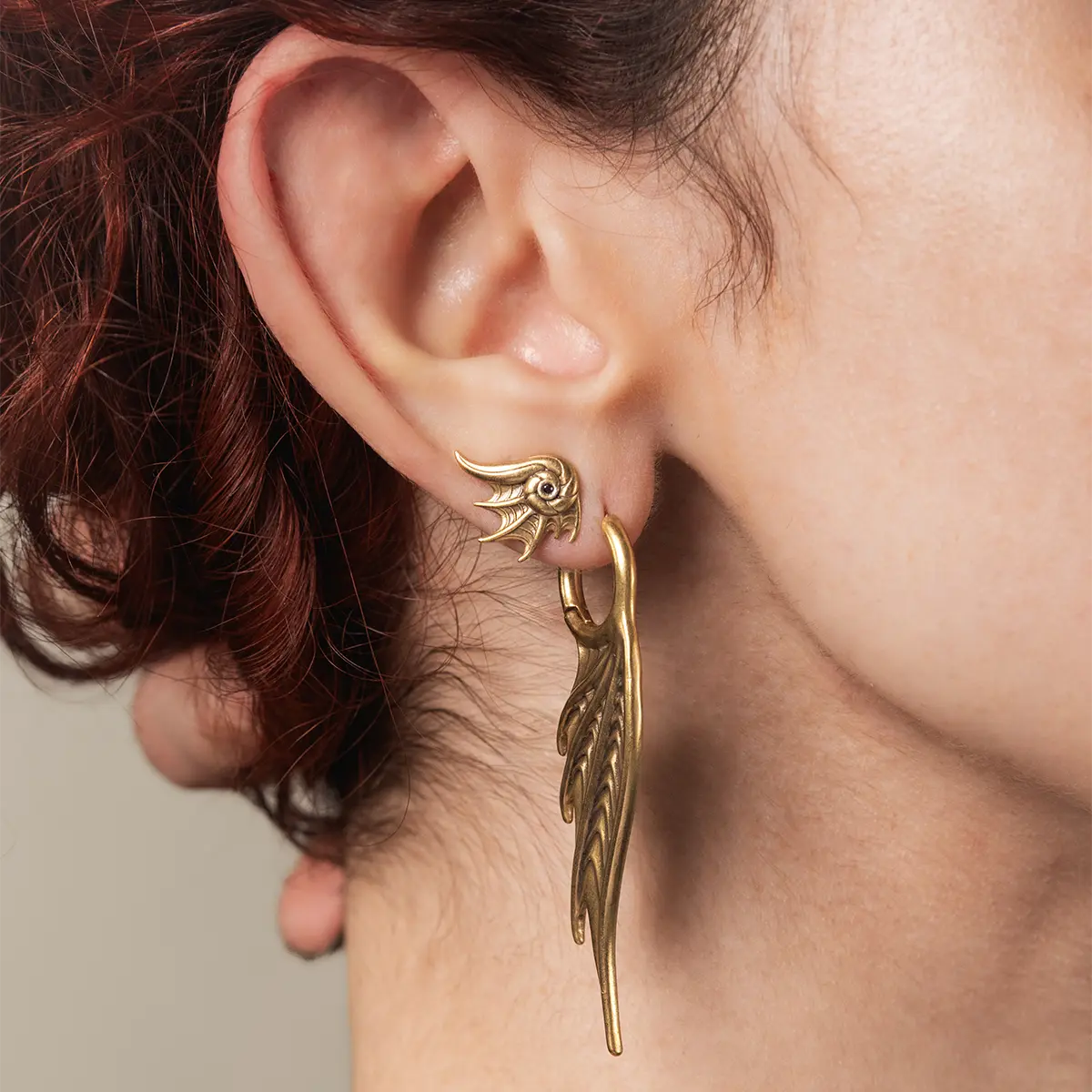 Model wearing the gold Abyss Conch Ear Studs, showing the curled sea-creature shape and dark stone center on the ear.