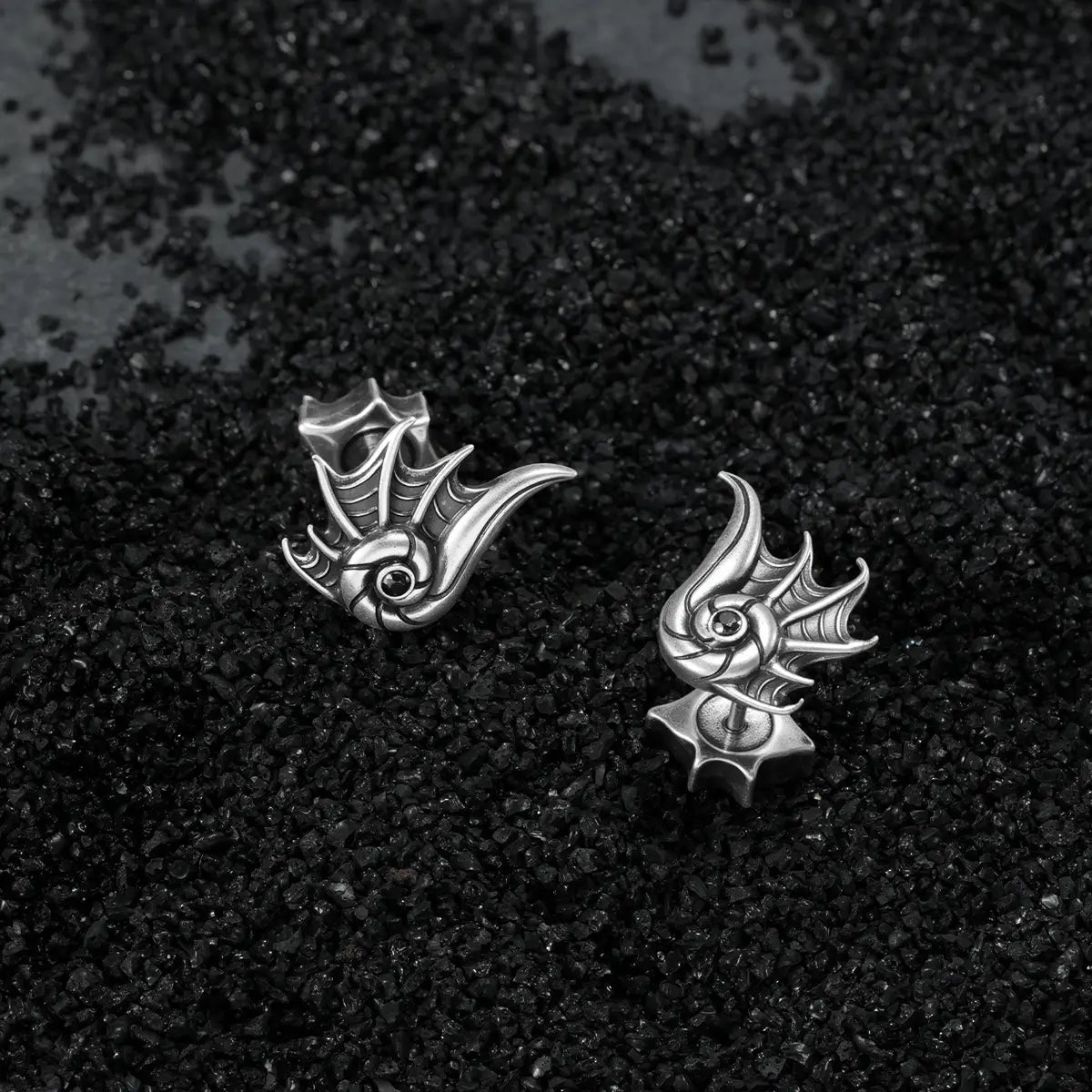 Silver Abyss Conch Ear Studs displayed on black sand, featuring sculpted conch ridges, black zircon centers, and ocean relic styling.
