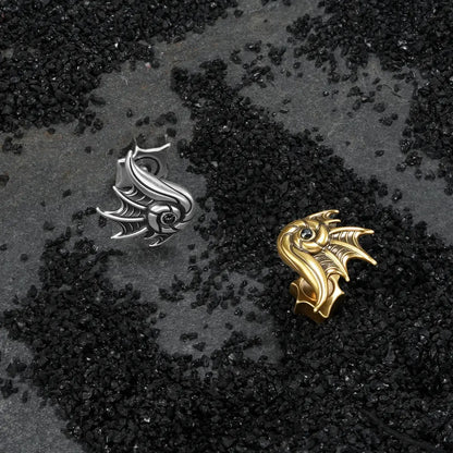 Silver and gold Abyss Conch Ear Studs displayed on black sand, showing the dark sea-creature forms and black zircon centers.