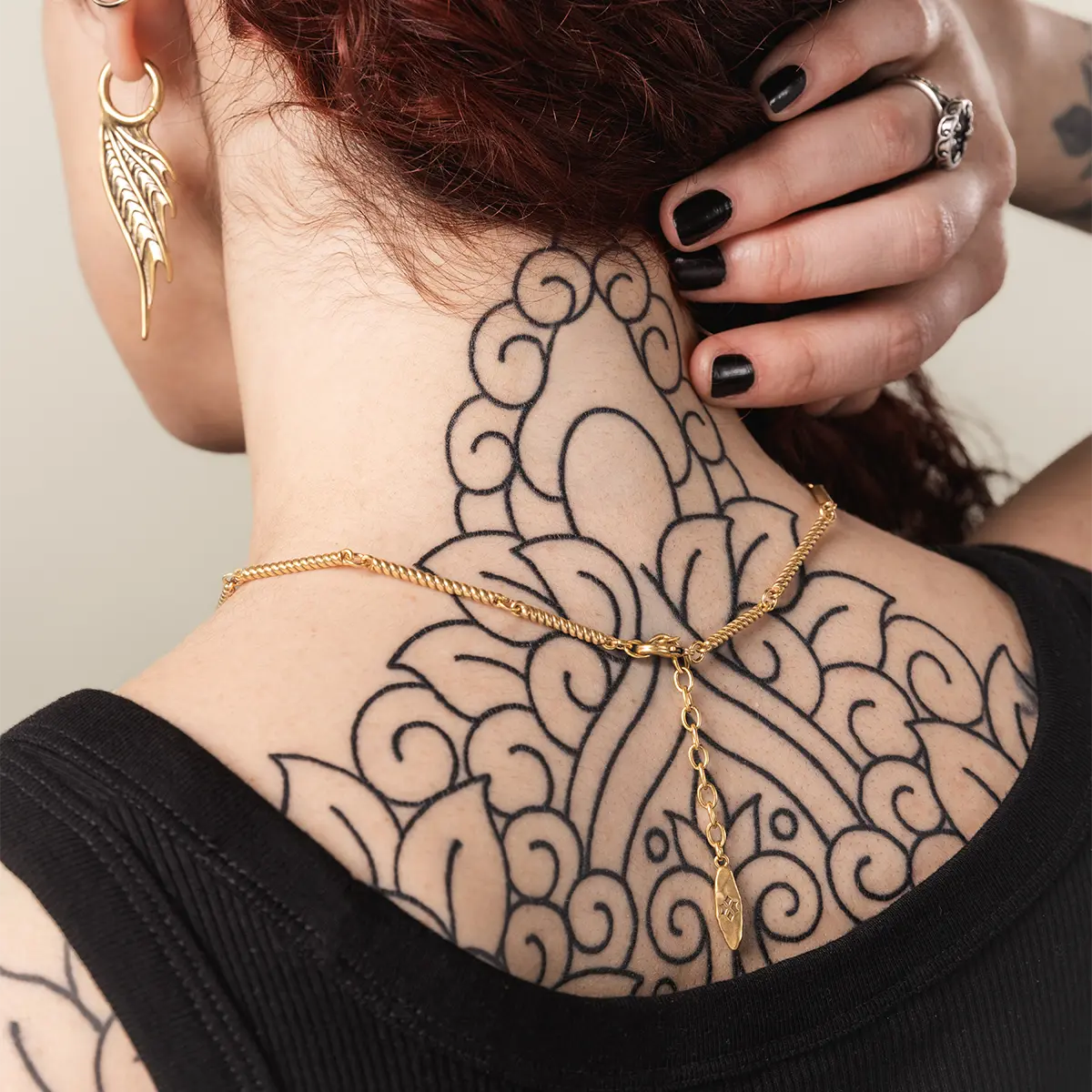 Model wearing the gold Abyssal Bind Necklace with matching ocean-inspired jewelry, styled with dark nails and back tattoo detail.