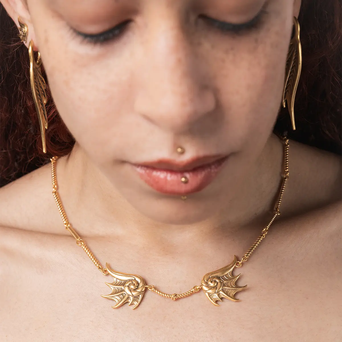 Model wearing the gold Abyssal Bind Necklace, showing the twin conch-like forms and central rope detail against the neck.