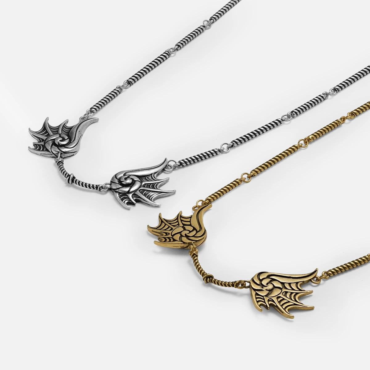 Silver and gold Abyssal Bind Necklaces shown together, featuring twin shell-like forms, central rope chain details, and sculptural ocean-inspired design.