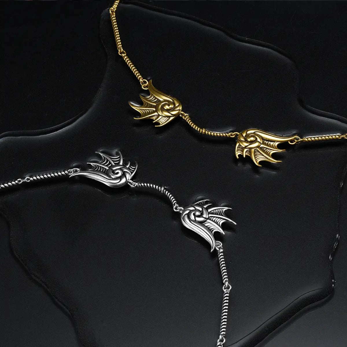 Silver and gold Abyssal Bind Necklaces displayed on a dark wet surface, showing the twin conch forms and ocean relic styling.