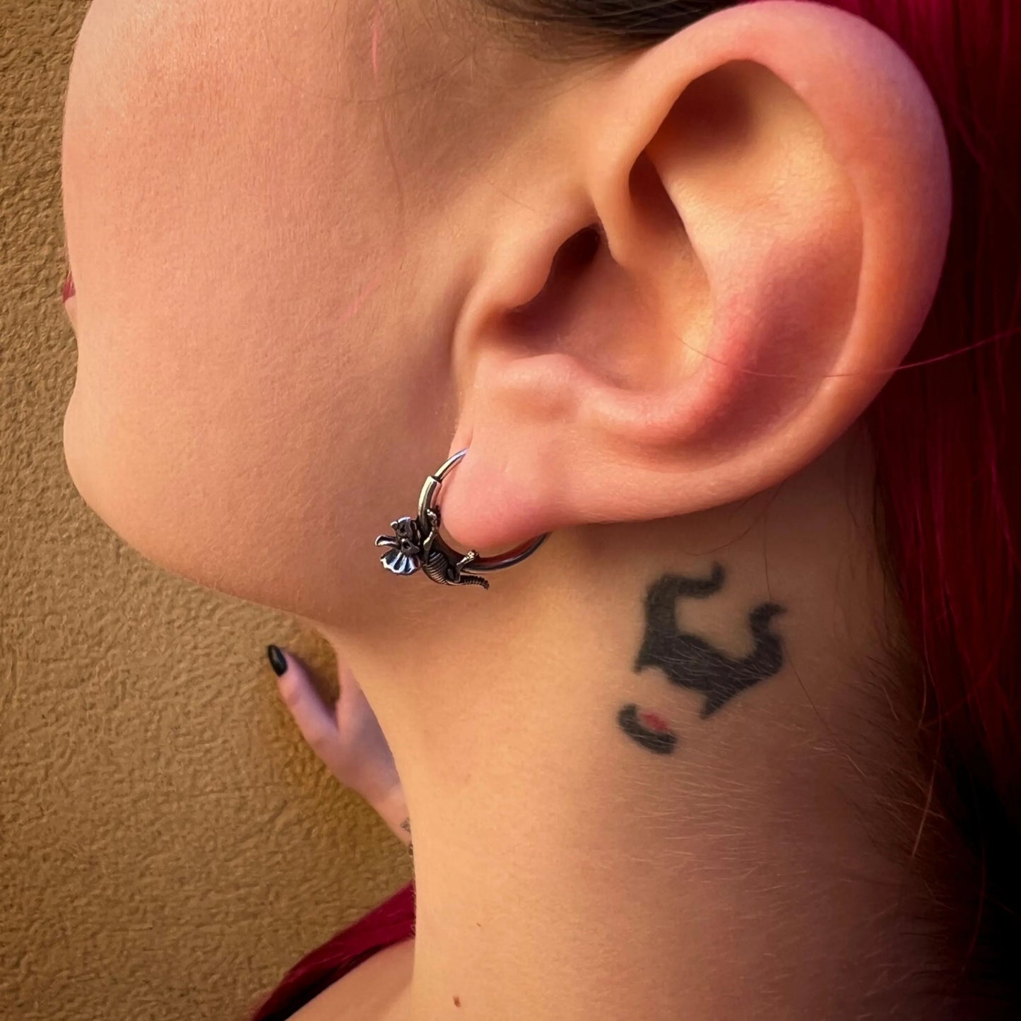 Model wearing a silver Adaptive Evolution hoop earring with small creature detail
