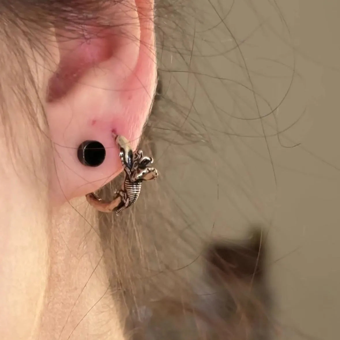 Model wearing silver Adaptive Evolution Earrings with dinosaur skeleton and frilled lizard hoop design