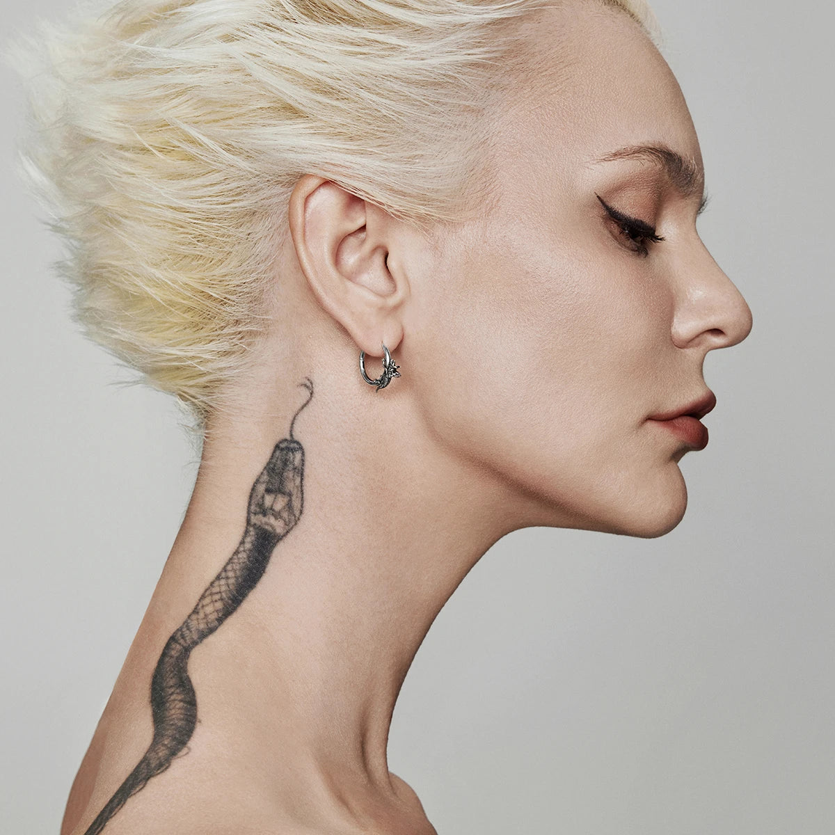 Profile view of a model wearing a small silver-tone hoop earring with an ornamental accent near the earlobe