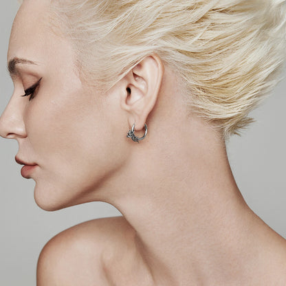 Side profile of a model wearing a silver-tone hoop earring featuring a small decorative floral element