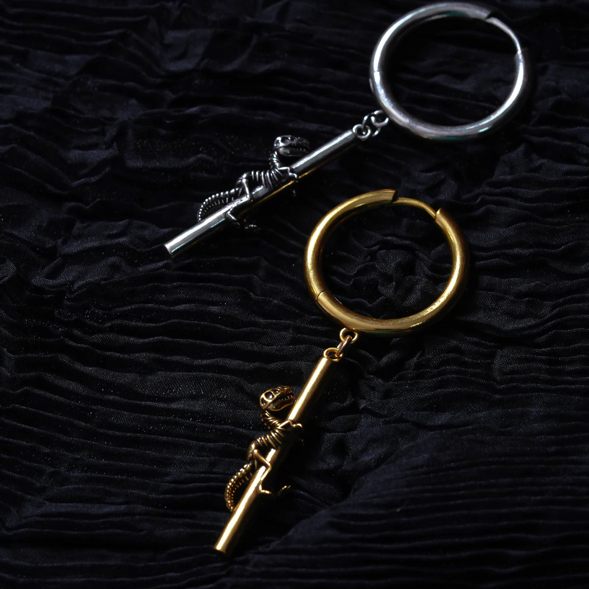 Silver-tone and gold-tone hoop earrings with dinosaur skeleton charms laid on dark fabric