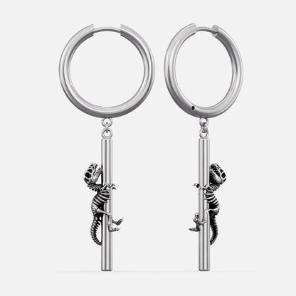 Silver-tone hoop earrings with a dangling dinosaur skeleton charm climbing a bar, shown as a pair