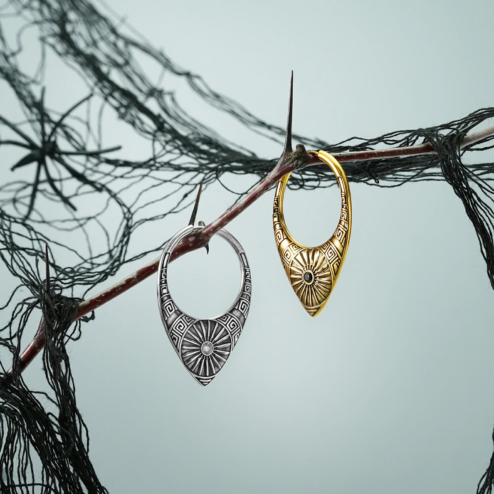 Silver and gold Ancient Sun hoop earrings hanging from a dark branch