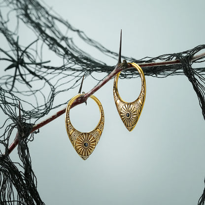 Pair of gold Ancient Sun hoop earrings hanging from a dark branch