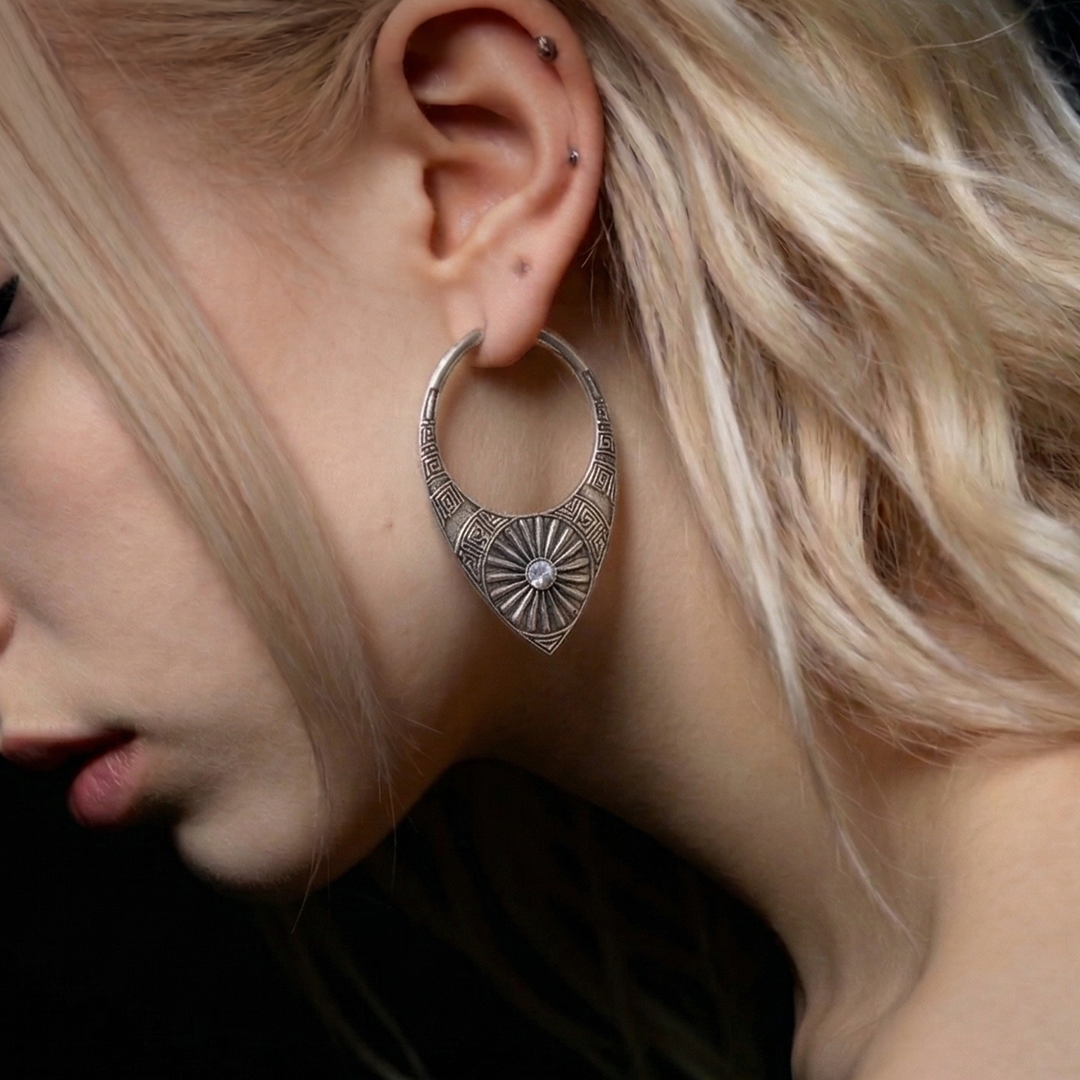 Close-up of a model wearing a silver-tone hoop earring with sunburst medallion design on the ear