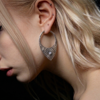 Close-up of a model wearing a silver-tone hoop earring with sunburst medallion design on the ear