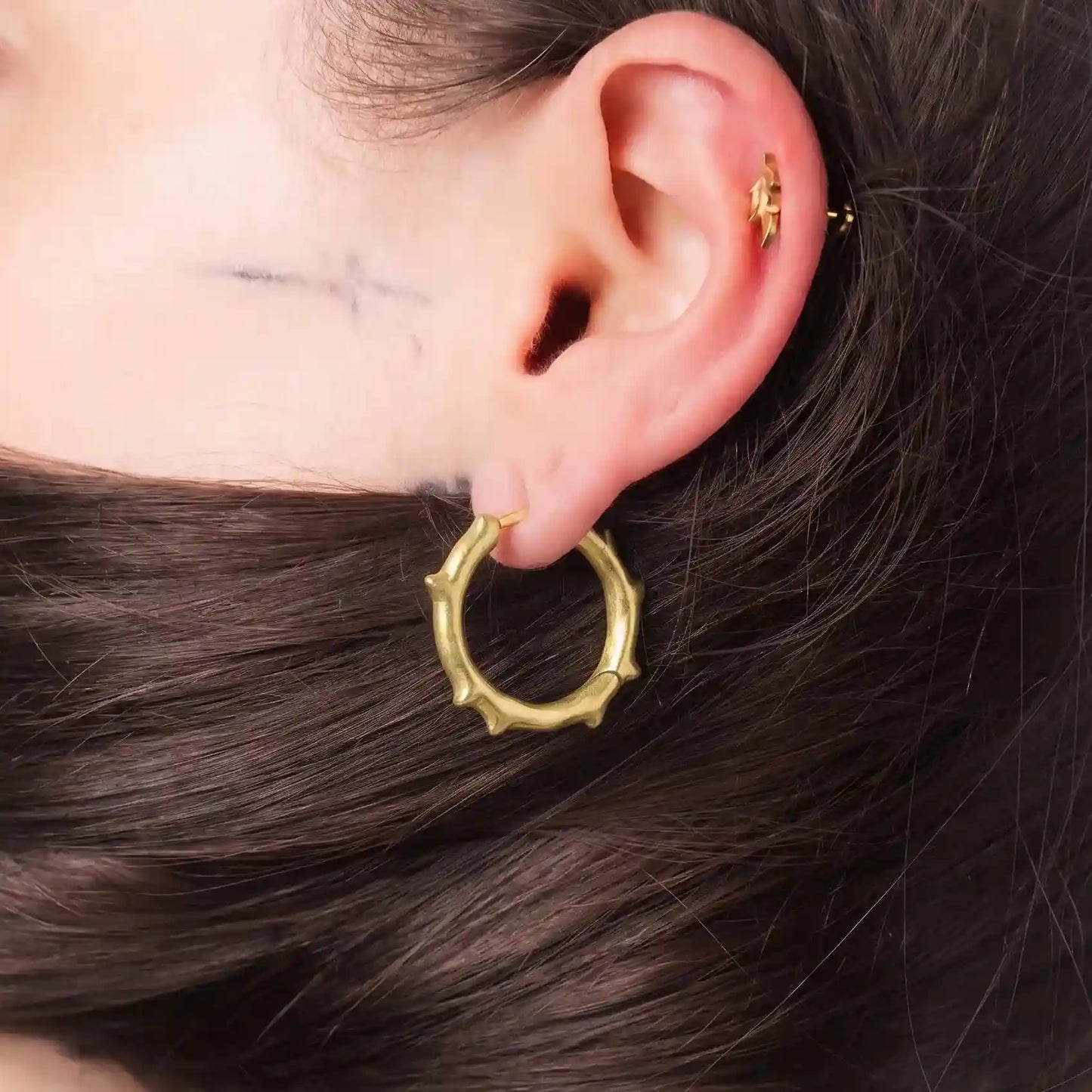 Model wearing gold Ancient Thorn Hoops with spiked thorn design and antiqued finish