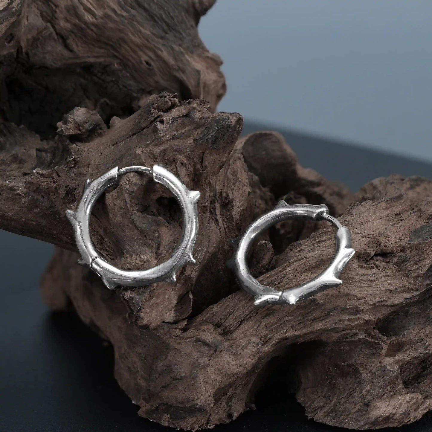 Close-up of silver Ancient Thorn Hoops on weathered wood with spiked hoop texture