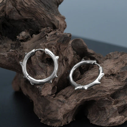 Close-up of silver Ancient Thorn Hoops on weathered wood with spiked hoop texture