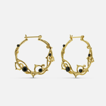 Pair of gold-tone vine hoop earrings with black stone accents on a plain background