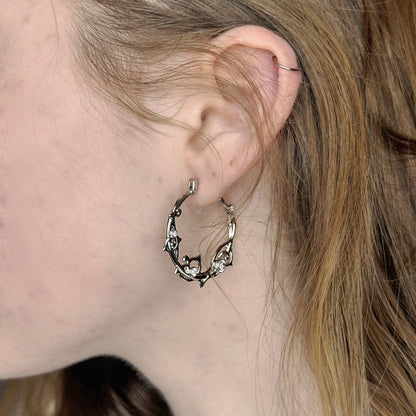 Close-up of a silver-tone vine hoop earring with clear stones worn on an ear