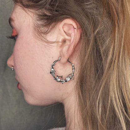 Silver-tone vine hoop earring with clear stones worn on a model's ear, side view