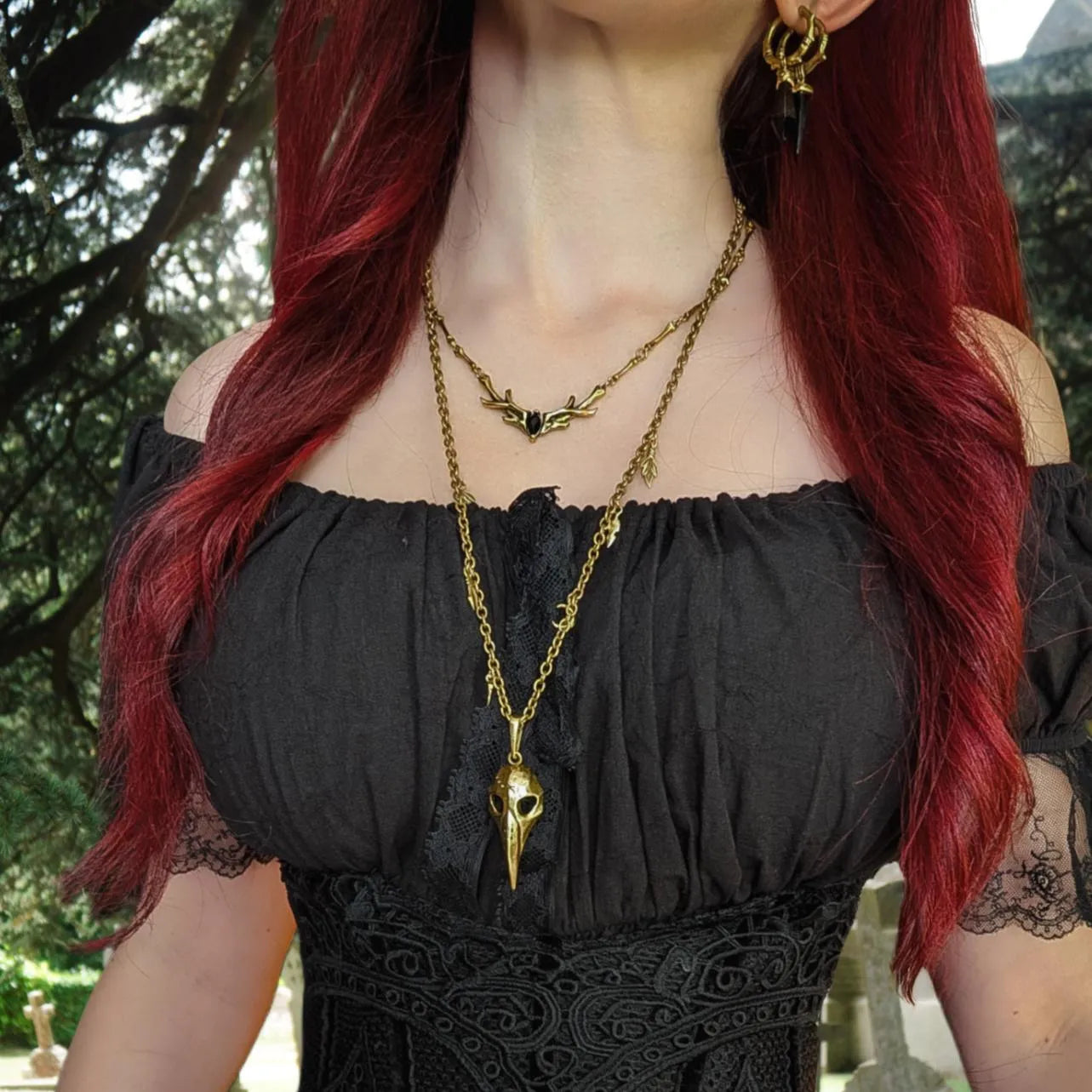 Model wearing the gold Augur Skull Necklace with bird skull pendant, leaf charms, curb chain, and dark forest-inspired styling.
