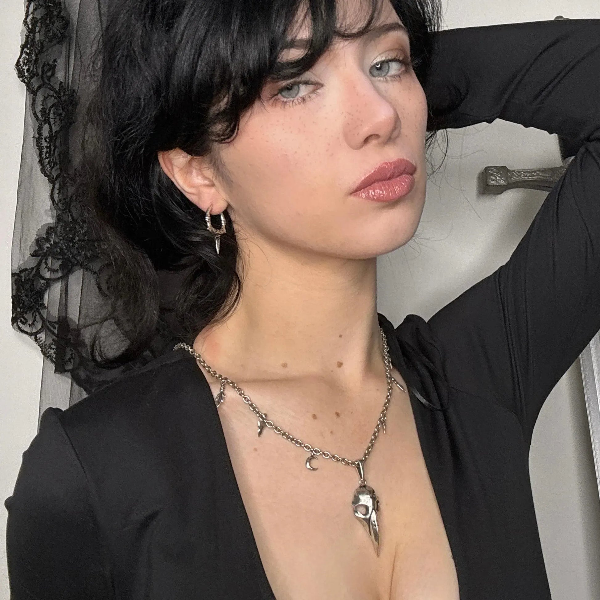 Model wearing the silver Augur Skull Necklace with bird skull pendant, leaf charms, curb chain, and dark gothic styling.