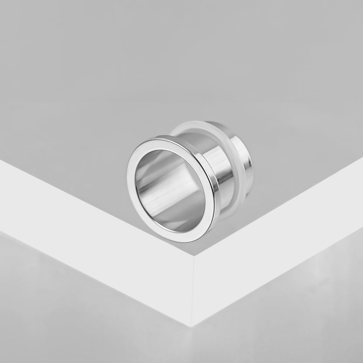 Polished silver Aurora ear tunnel resting on the edge of a white display block