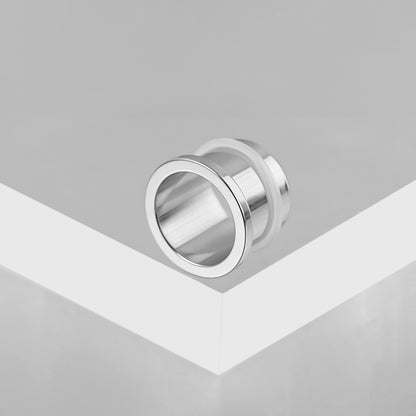 Polished silver Aurora ear tunnel resting on the edge of a white display block