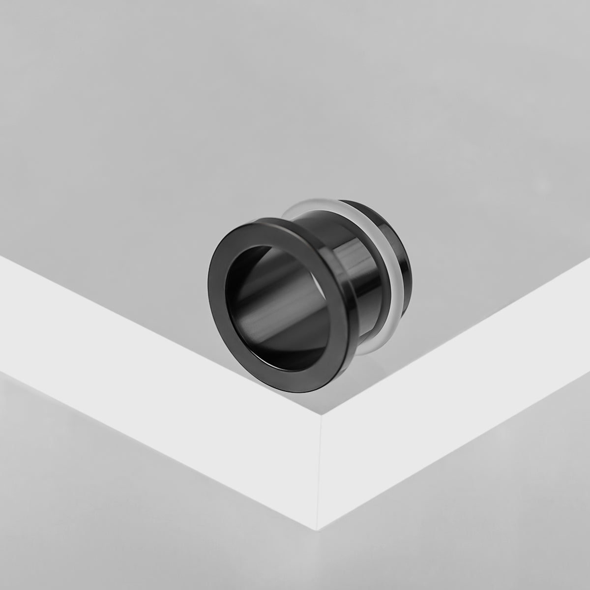 Black Aurora ear tunnel resting on the edge of a white geometric display block