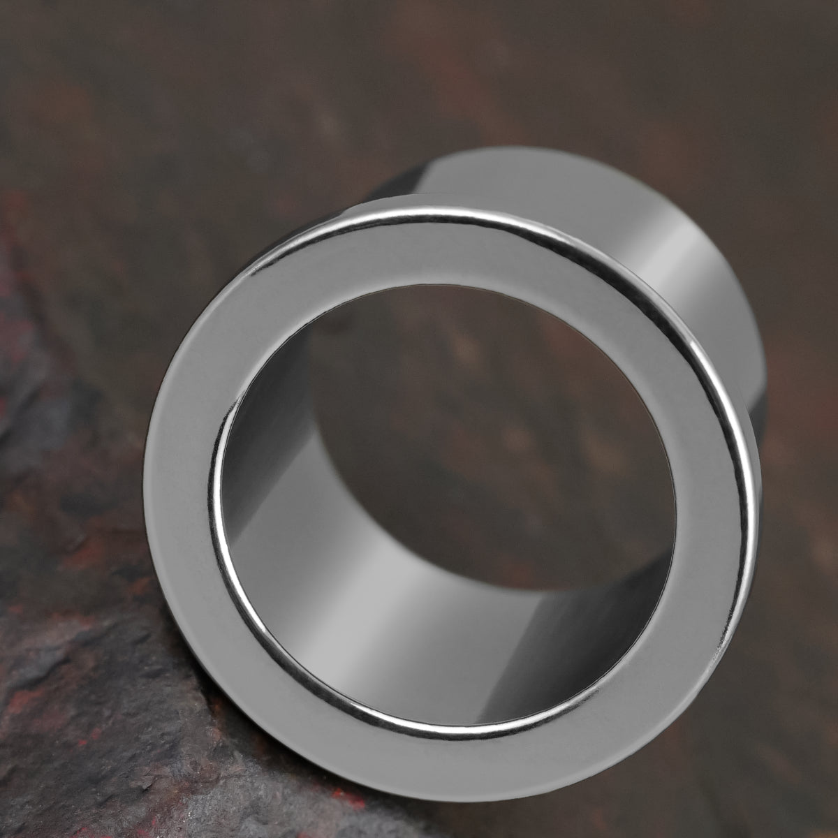 Macro view of a polished silver Aurora ear tunnel showing its rounded flared rim and inner channel