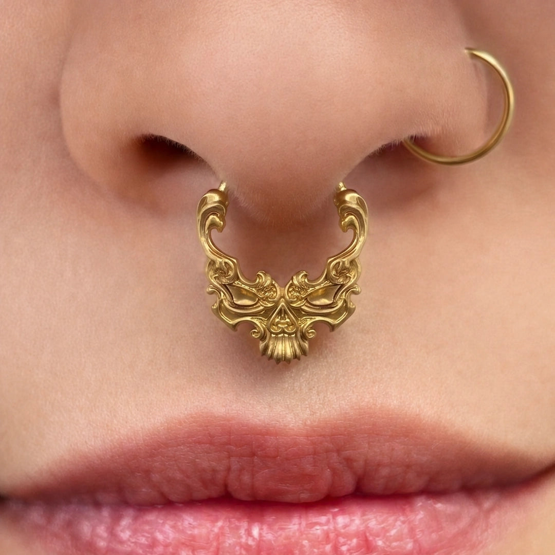 Gold-tone Baroque Skull Clicker worn as a septum ring, showing its detailed skull-inspired silhouette.