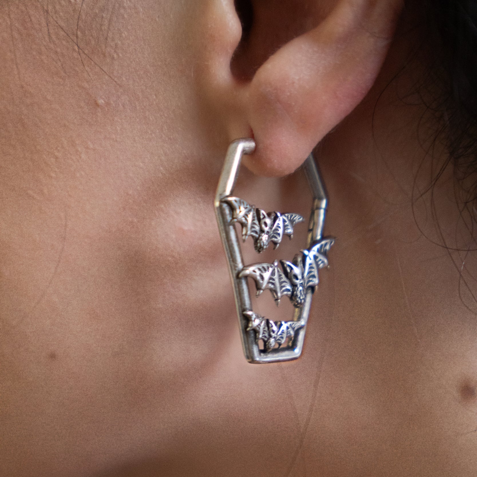Close-up of a coffin-shaped hoop earring with bat charms worn on a model's ear
