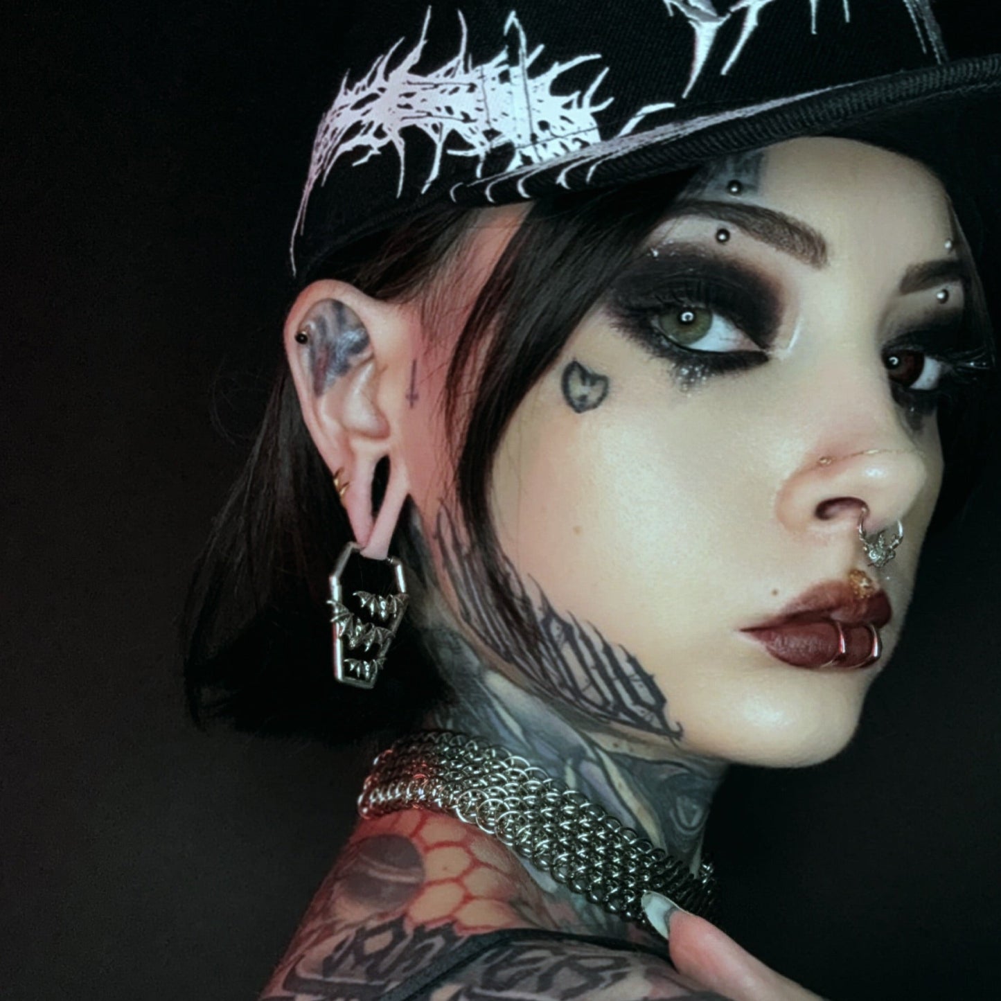 Model wearing a silver Bat Tomb coffin earring below a black ear plug