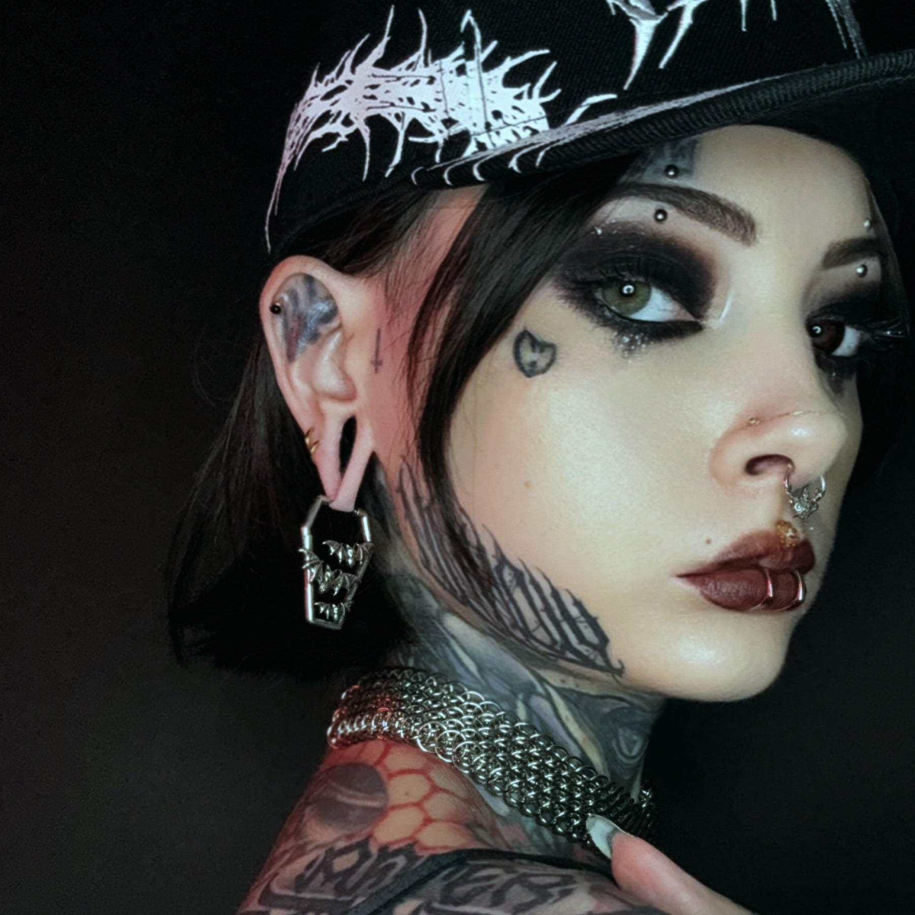 Model wearing a silver Bat Tomb coffin earring below a black ear plug