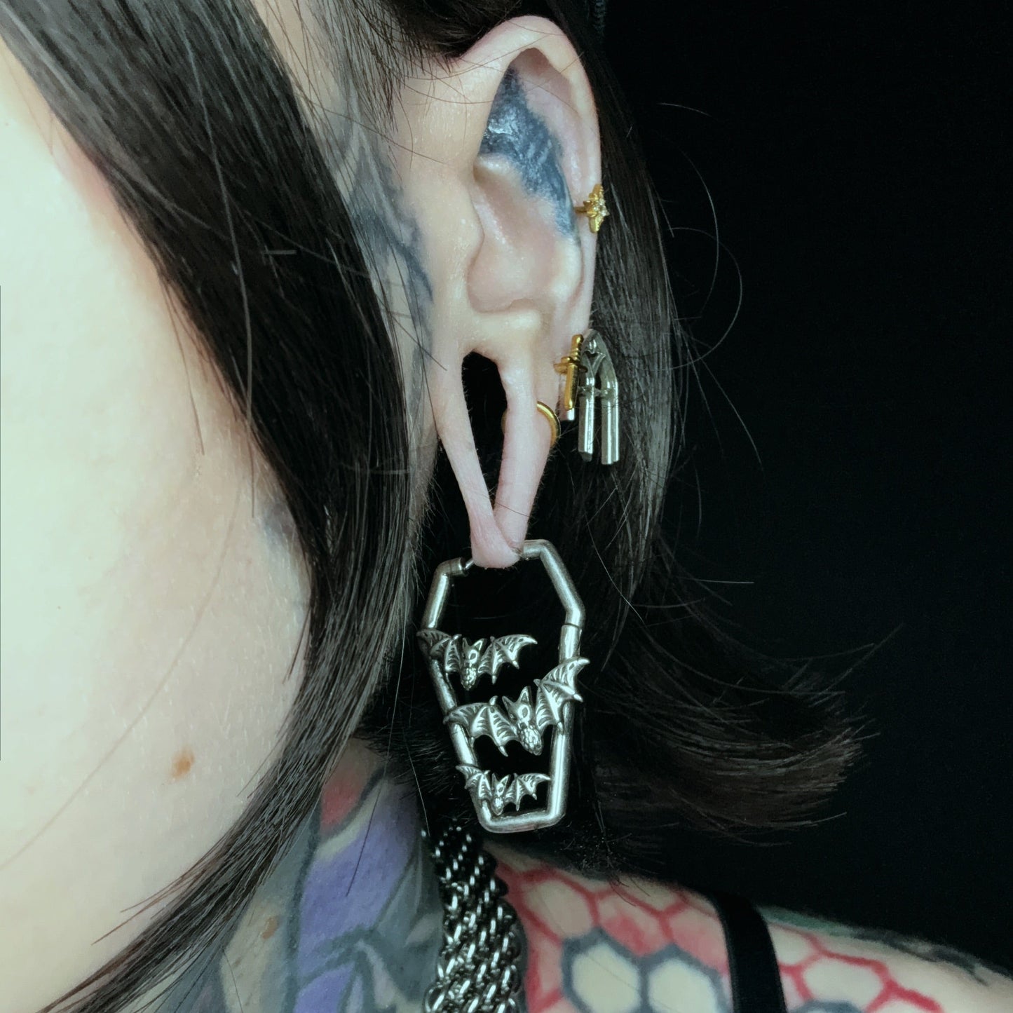 Close-up of silver Bat Tomb coffin earring worn with multiple ear piercings