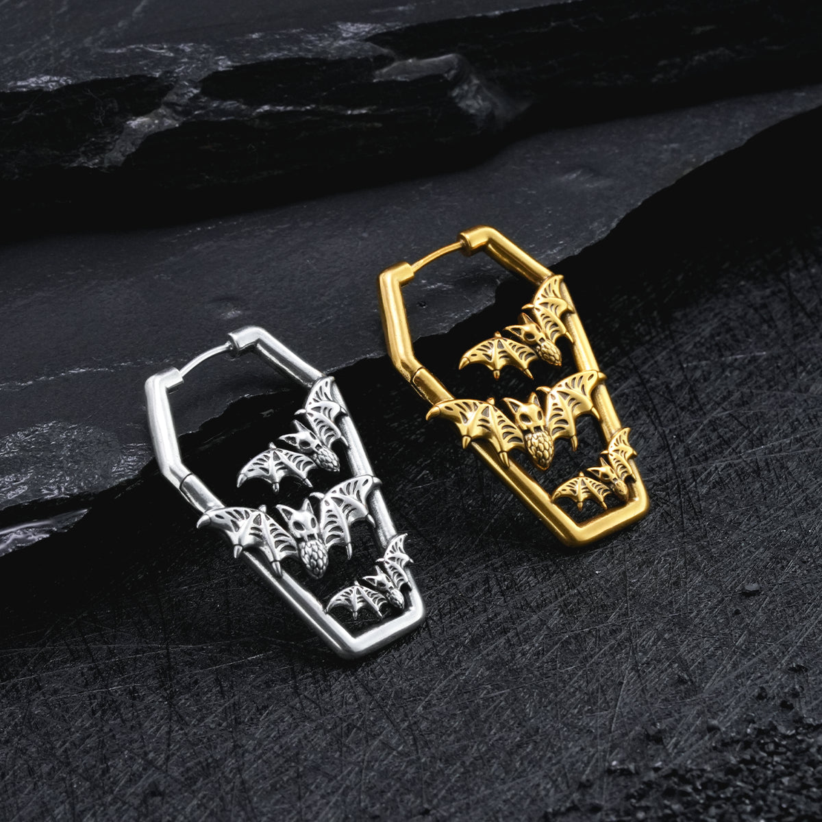 Silver and gold Bat Tomb coffin hoop earrings displayed on dark stone