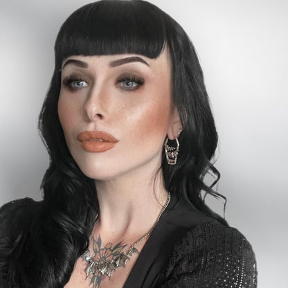 Model with dark hair wearing a silver-tone coffin-shaped bat charm earring and matching bat necklace