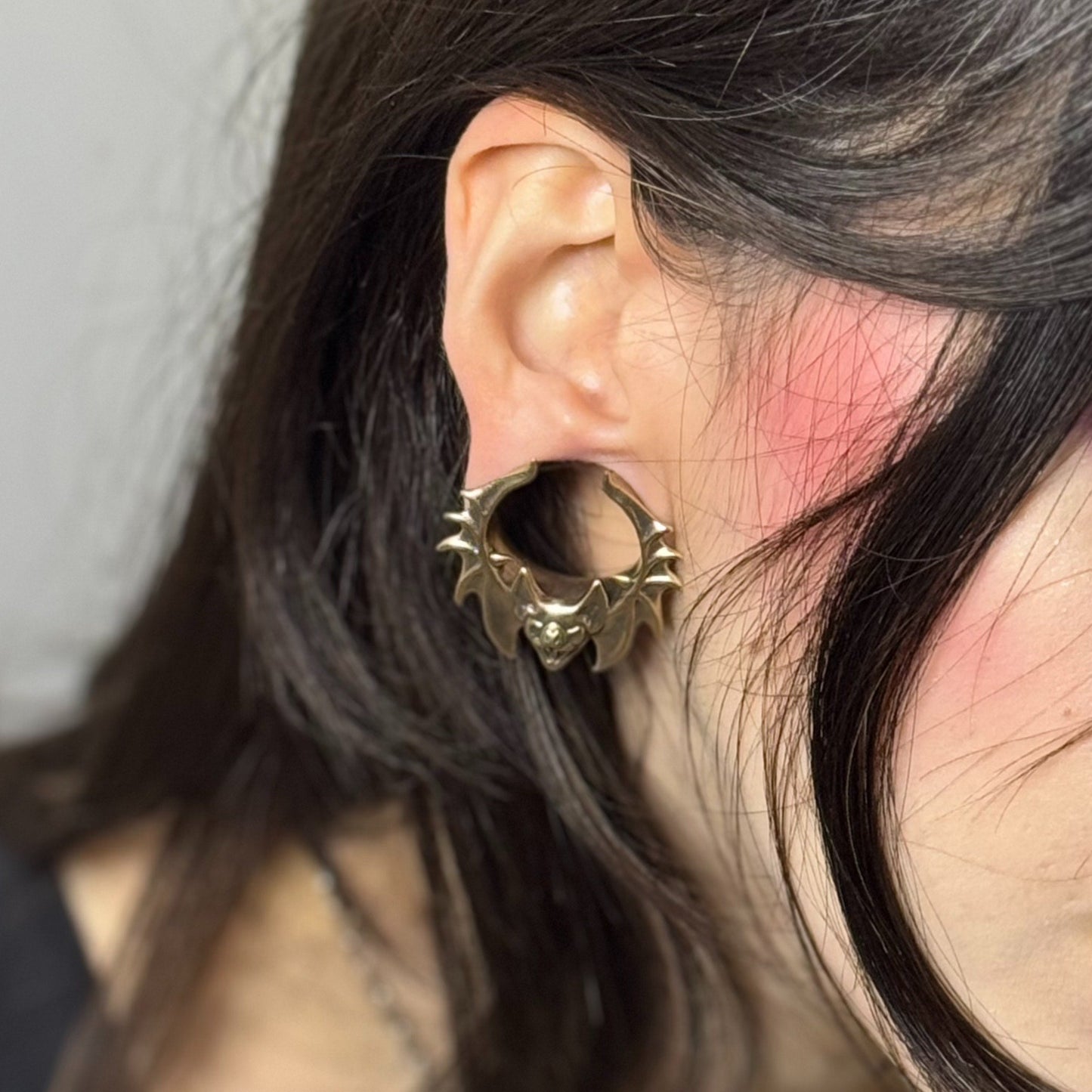 Close-up of gold Bat Whisper tunnel worn in a stretched lobe
