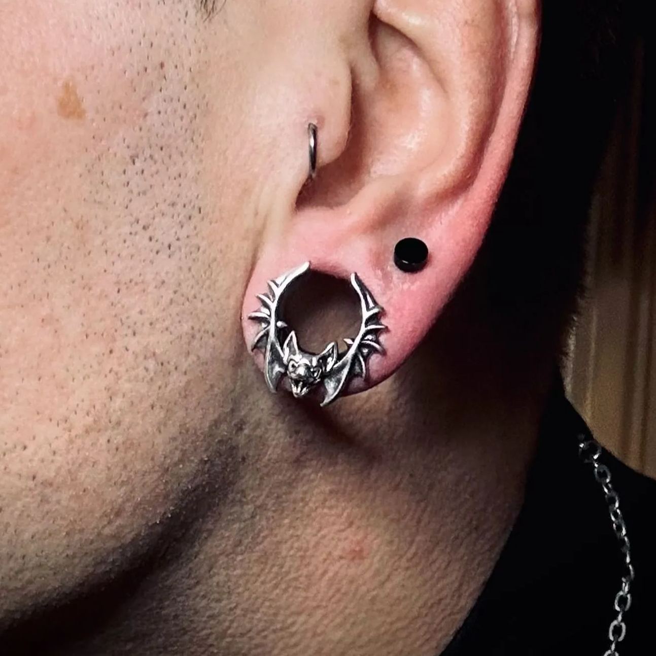 Close-up of an ear with a silver-tone bat tunnel earring and a black stud piercing