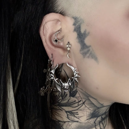 Close-up of a tattooed ear wearing a silver-tone bat tunnel earring with dangling cross charms