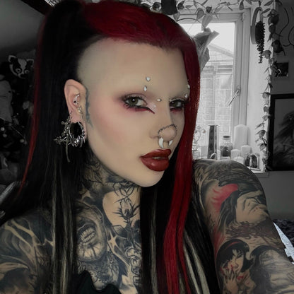 Person with tattoos wearing a silver-tone bat-shaped tunnel earring alongside multiple ear piercings