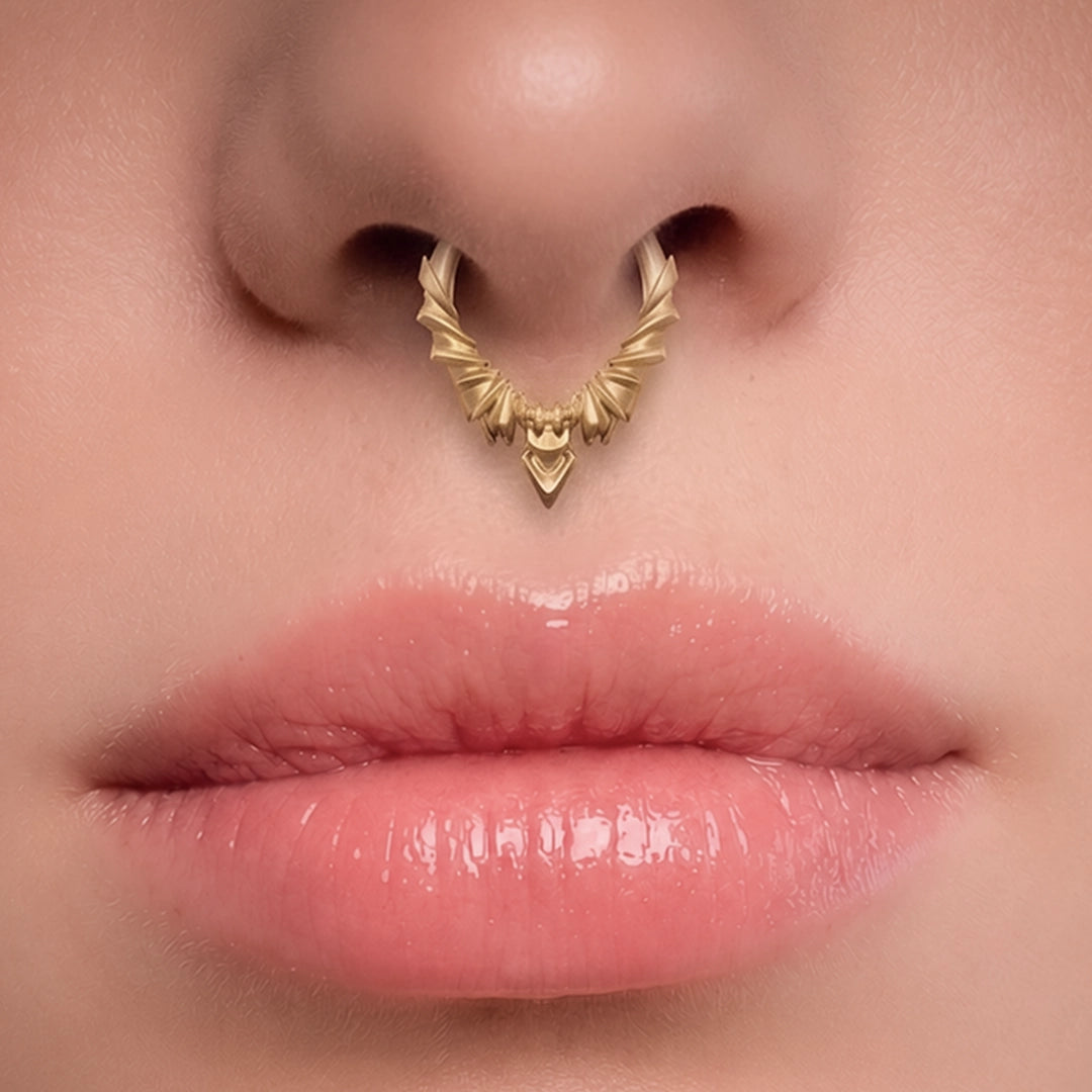 Gold-tone Bat Wing Clicker worn as a septum ring, showing its sharp wing-inspired silhouette.