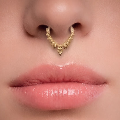 Gold-tone Bat Wing Clicker worn as a septum ring, showing its sharp wing-inspired silhouette.