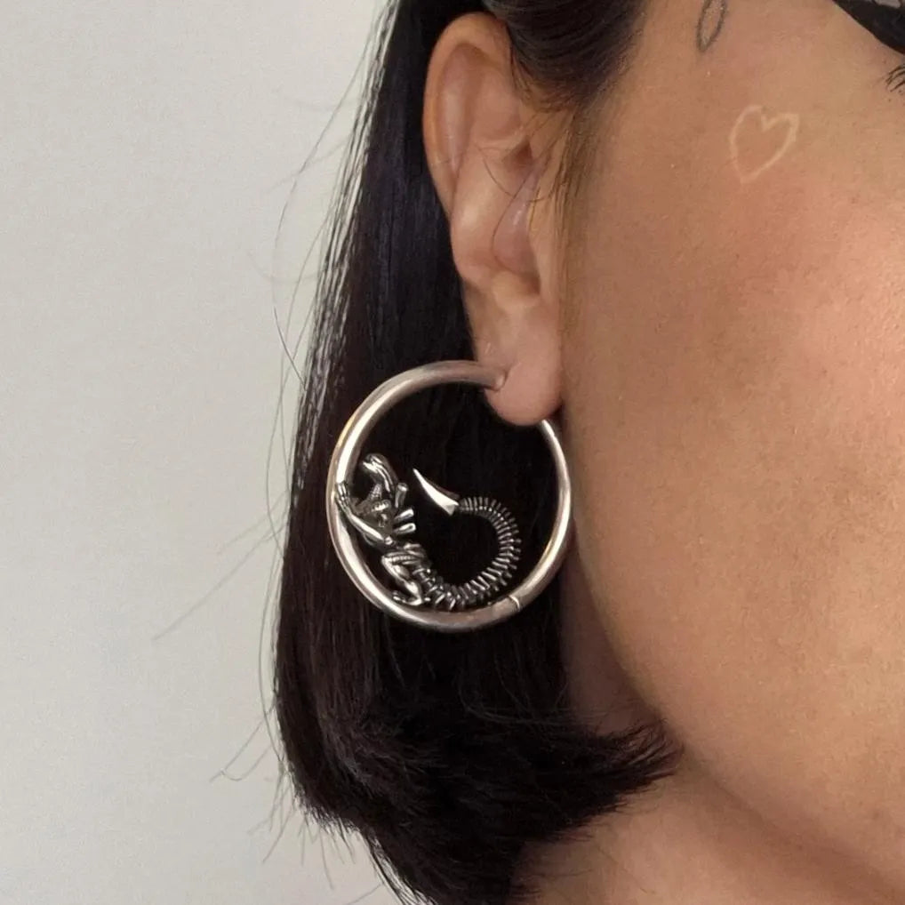 Model wearing silver Biomechanical Alien Hoop Earrings with alien figure and gothic sci-fi hoop design