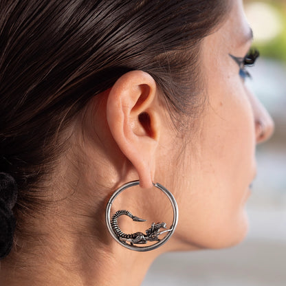 Silver-tone hoop earring with a biomechanical alien creature detail, worn by a model, close-up side view