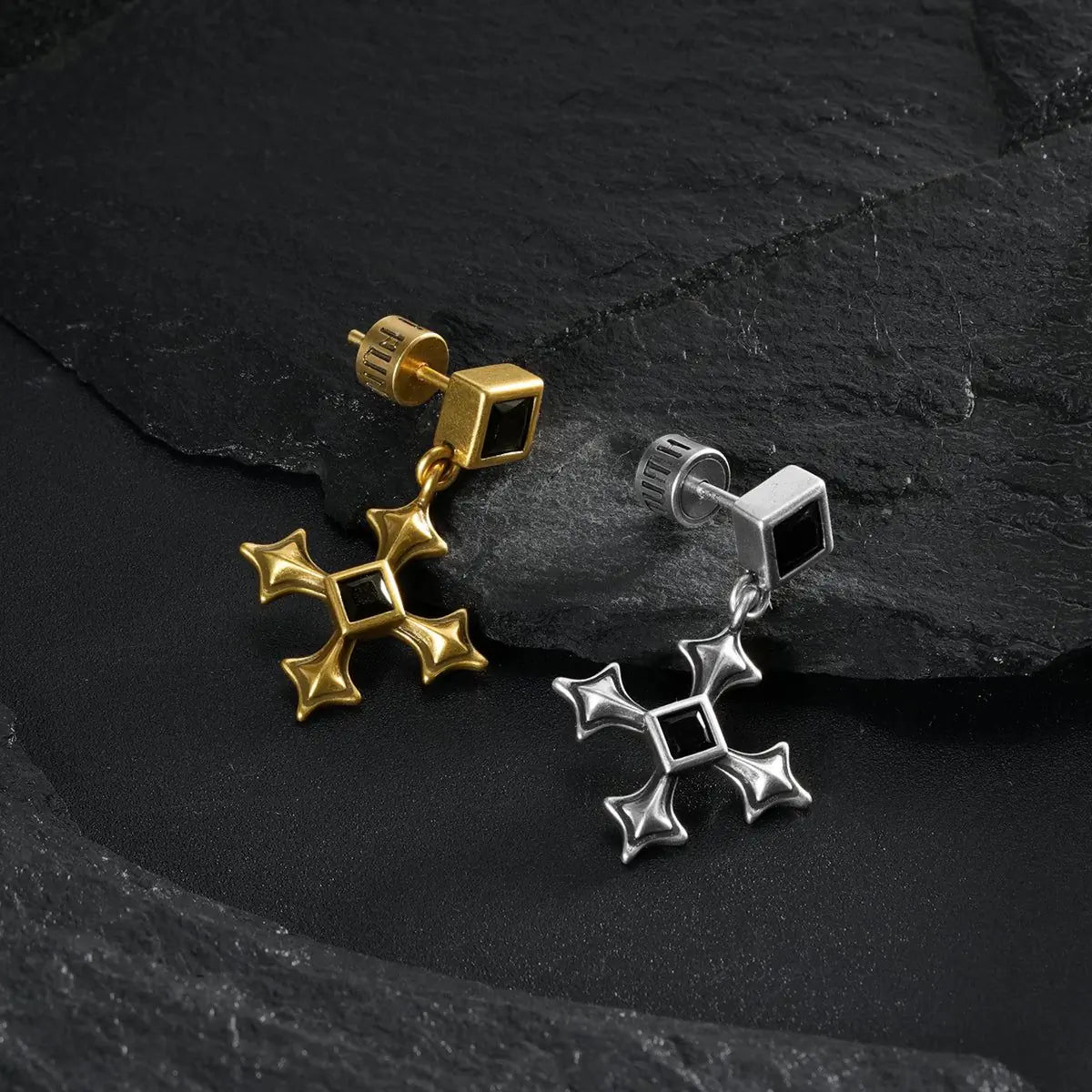 Silver and gold Black Testament Earrings arranged at angles on black textured fabric.