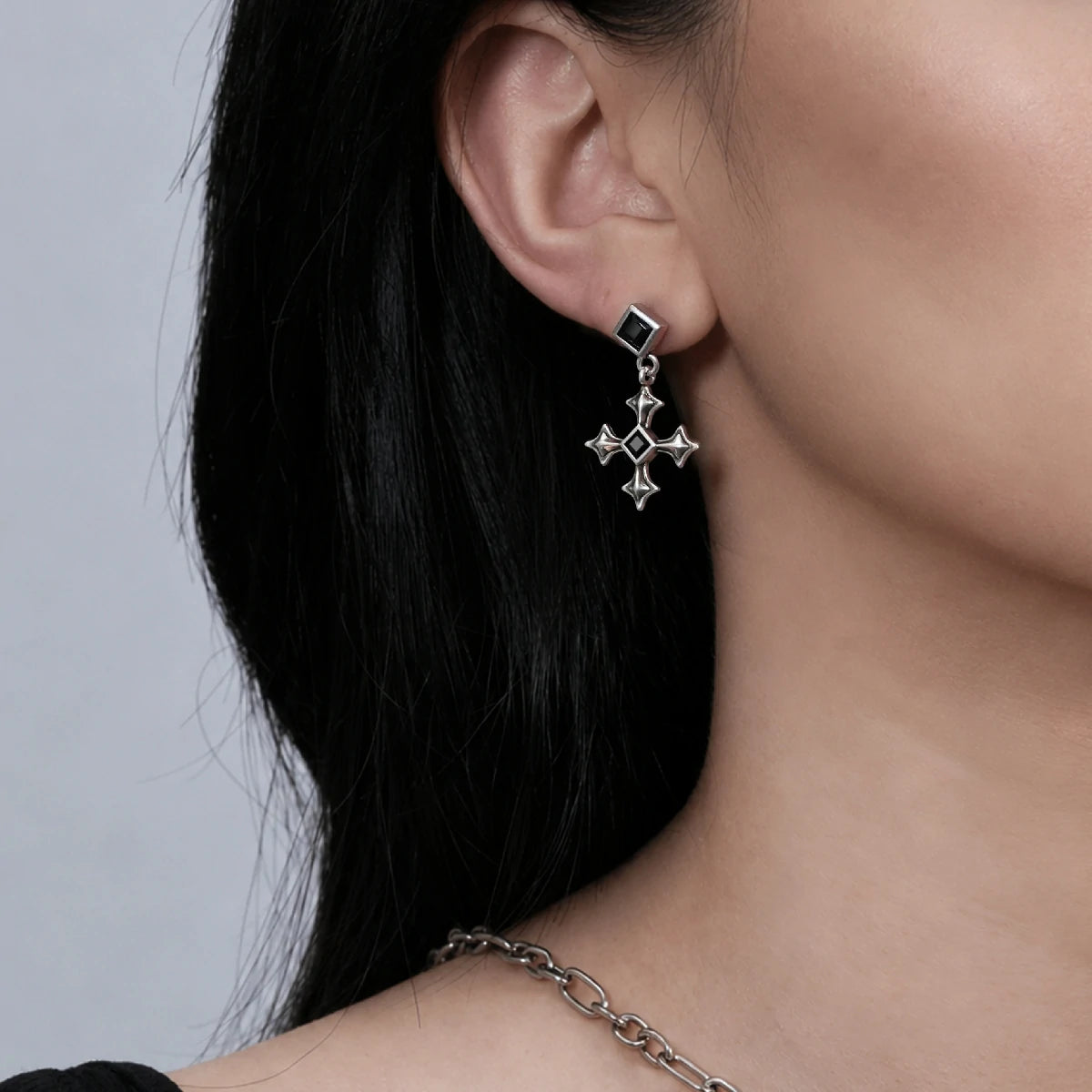 Black Testament Earrings in antiqued silver worn on the ear in a close side-neck view with dark hair swept back.