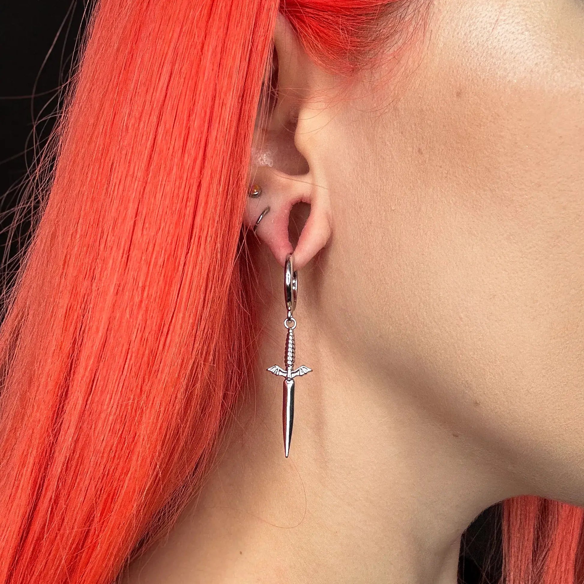blade wing earrings shown on a model in side view, featuring silver sword drop hoop earrings with wing accents